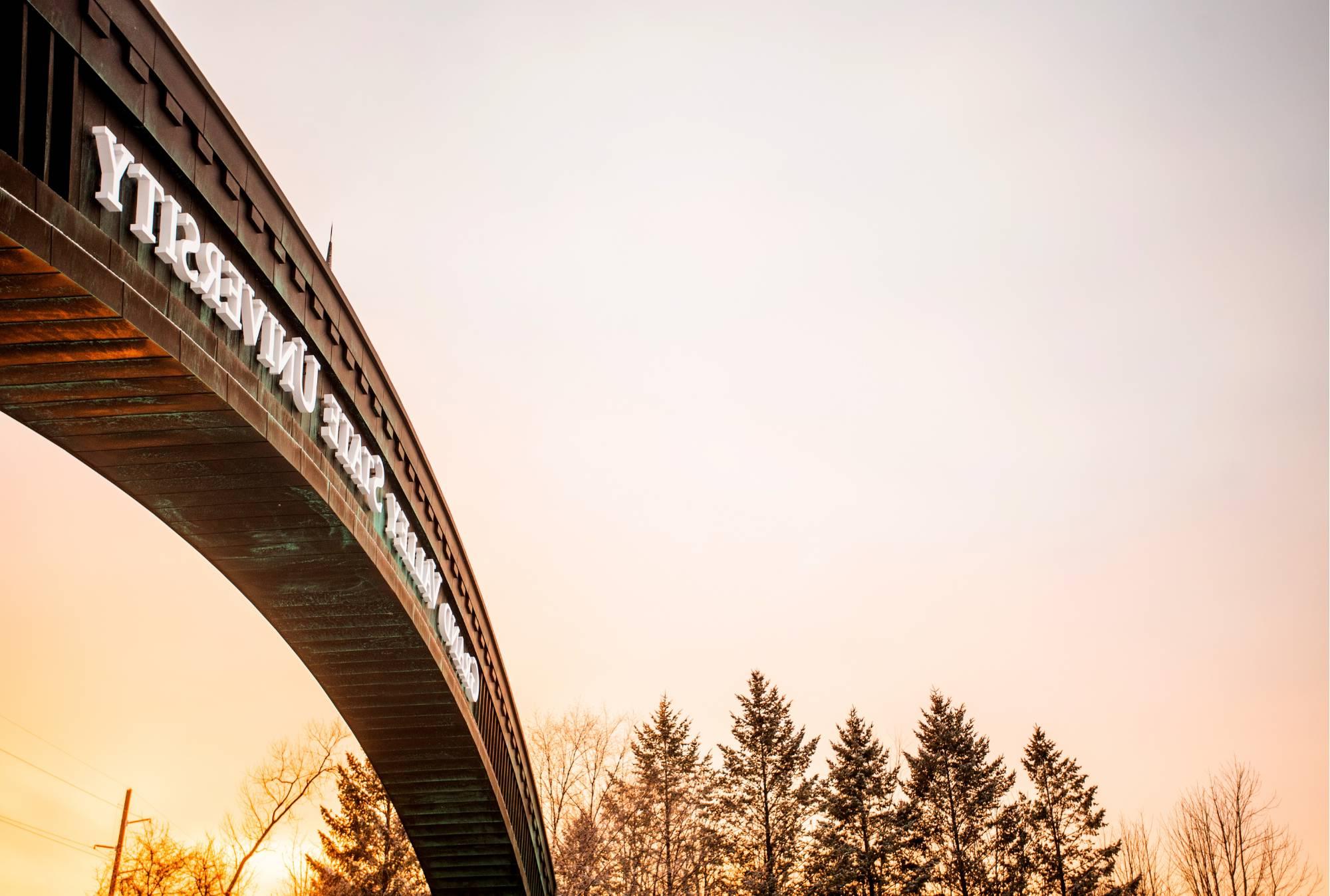 The Grand Valley State University Arch off Lake Michigan Drive that leads into north campus is pictured at sunrise. The sky is pink and orange.